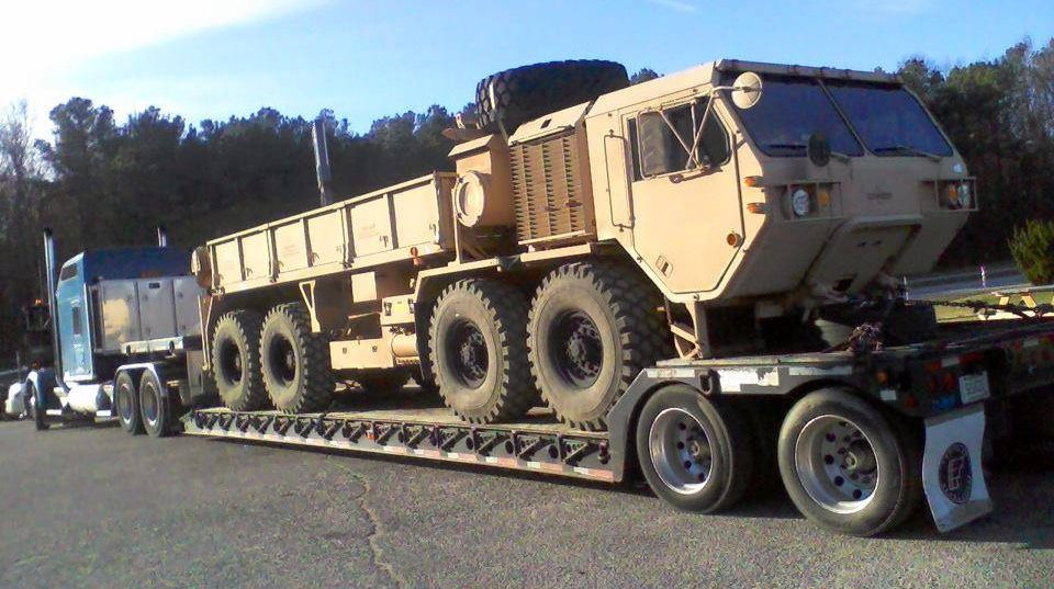 Tan military cargo truck on flatbed trailer